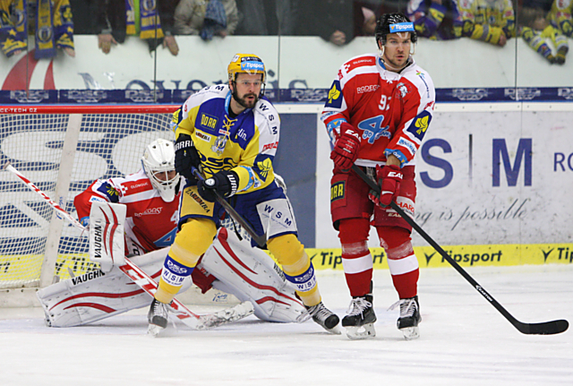 Branislav Konrád v brance HC Olomouc sleduje střelu zpoza loni olomouckého Martina Cibáka v dresu Zlína. Tomáš Valenta zase hrál za Zlín a nyní brání v dresu Kohoutů.